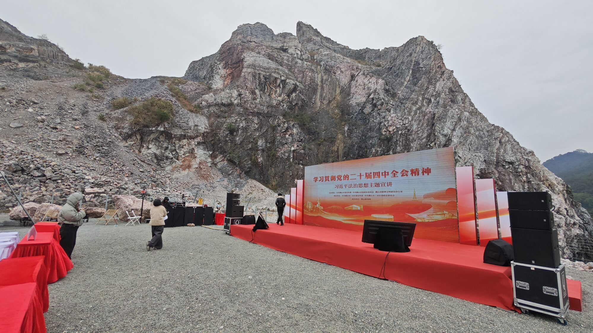 舞台与矿坑：红色地毯、LED 主题主屏，脚下是碎石地坪，身后是废弃采石场留下的崖壁