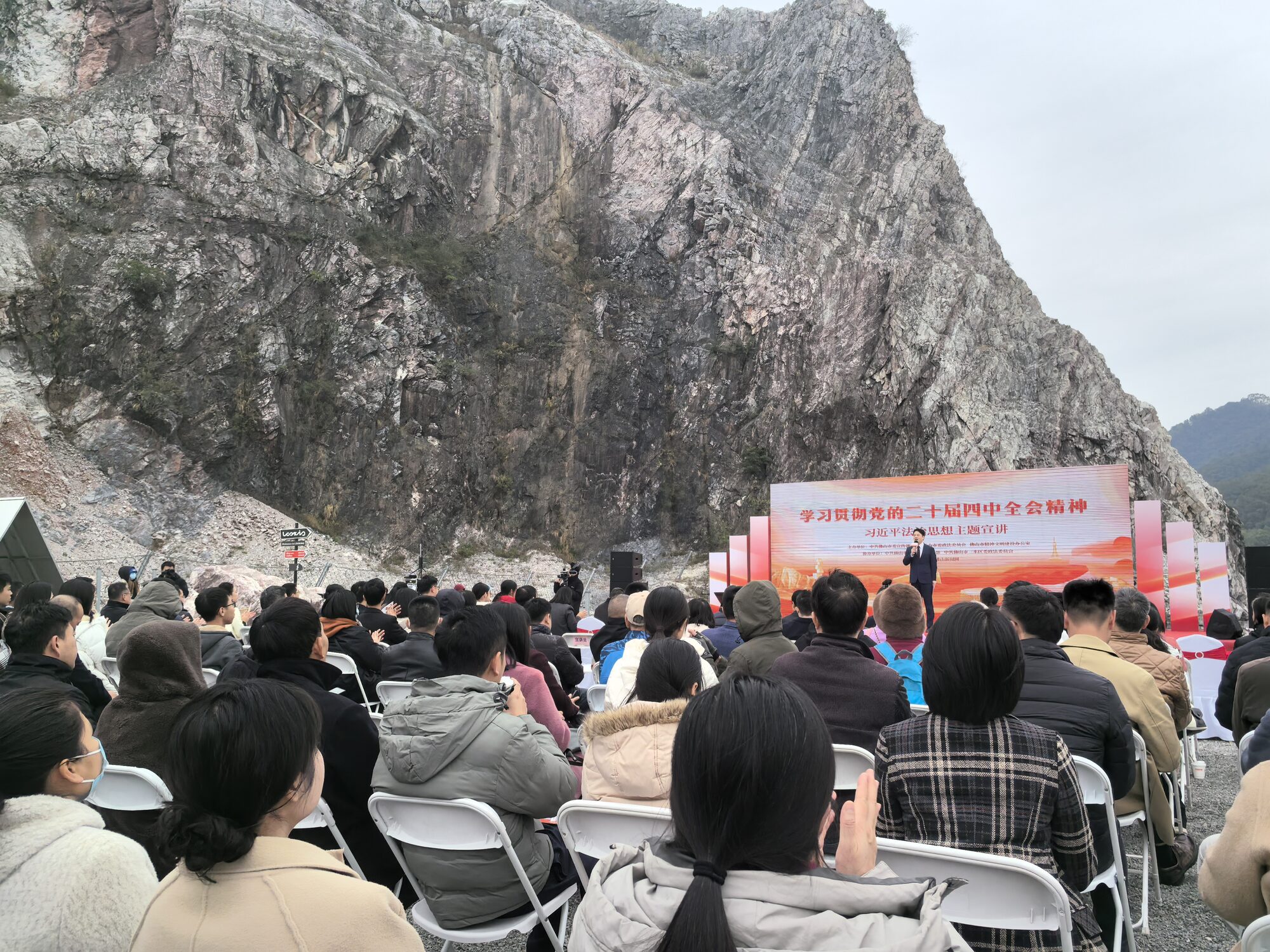 政务宣讲：观众席设在矿坑地坪上，前方是红色舞台与 LED 主题主屏，背后是裸露的石灰岩崖壁